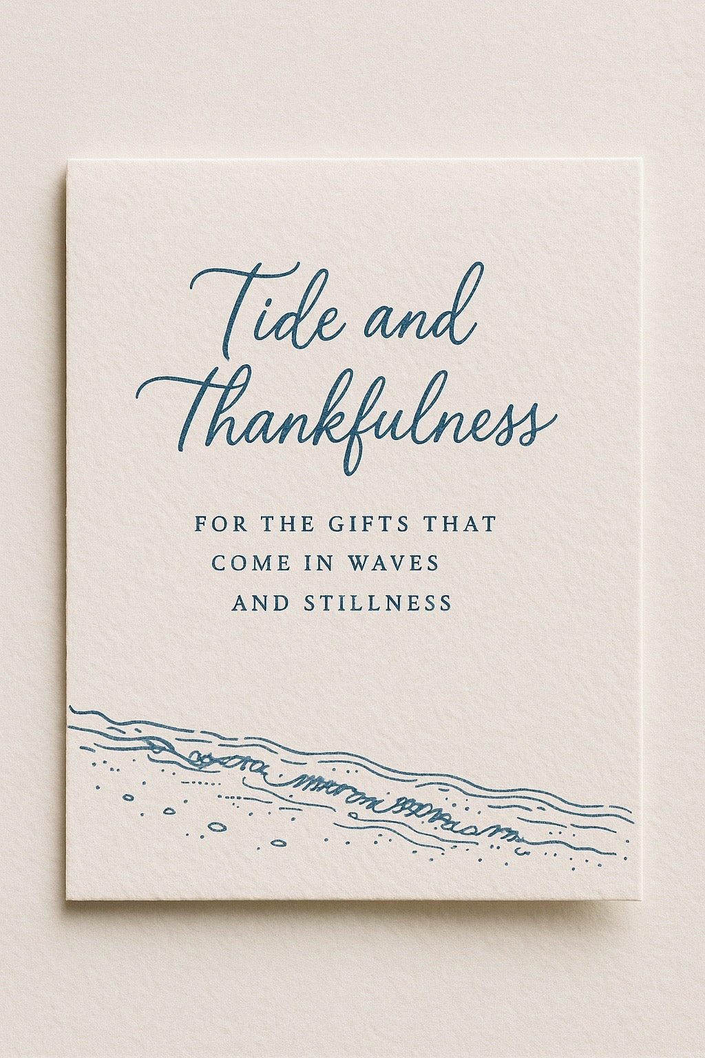 Cream-colored card with coastal blue script reading “Tide and Thankfulness,” featuring a minimalist shoreline illustration. The design evokes calm, gratitude, and coastal simplicity, styled on textured paper.